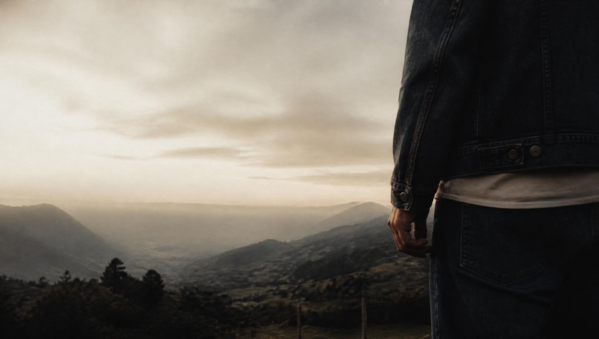 Figura en denim oscuro sobre un paisaje rural colombiano al amanecer.